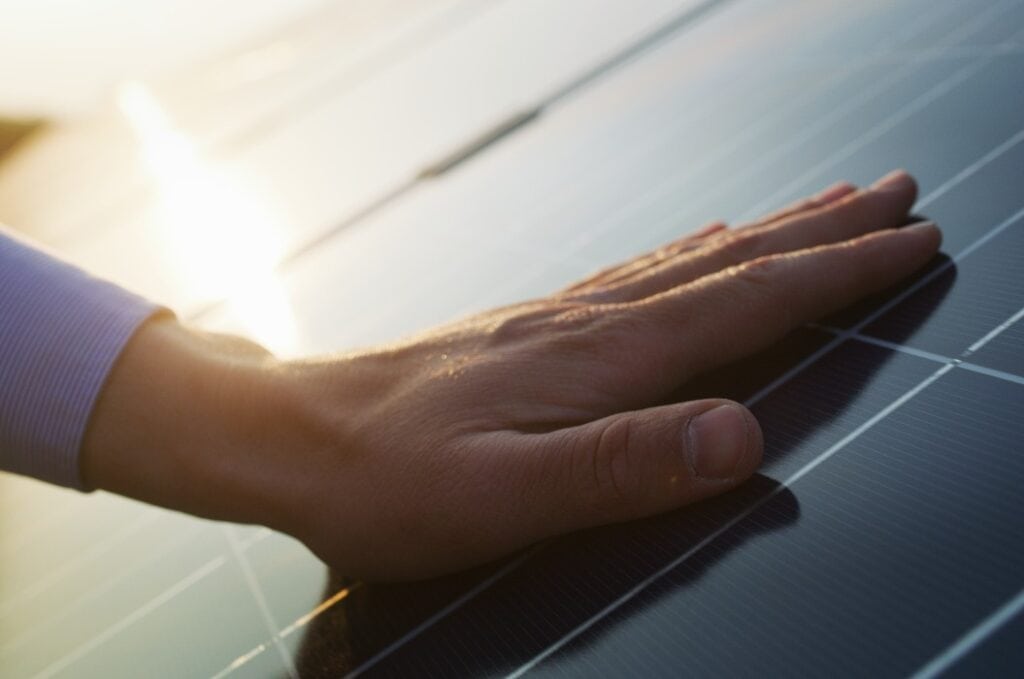 Close up of an young engineer hand is checking an operation of sun and cleanliness of photovoltaic solar panels on a sunset.Concept:renewable energy, technology,electricity,service, green,future