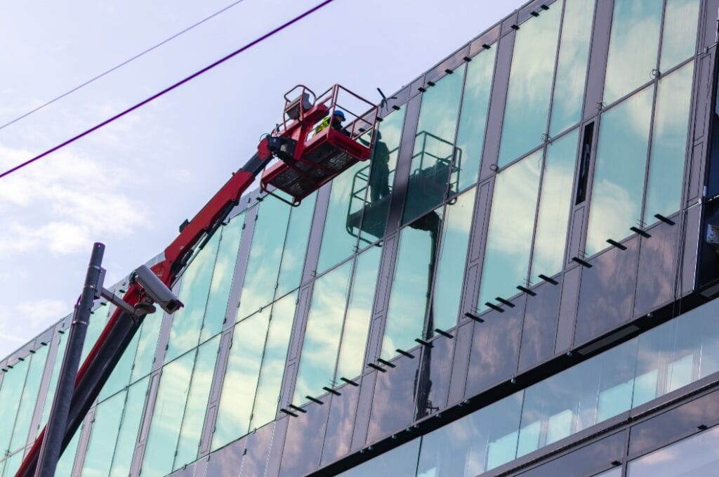 Sachverständige Bauarbeiter prüfen die Glasfassade eines neuen Gebäudes und führen die Bauabnahme inkl. Qualitätskontrolle und Mängelbeseitigung mit einem Kran durch
